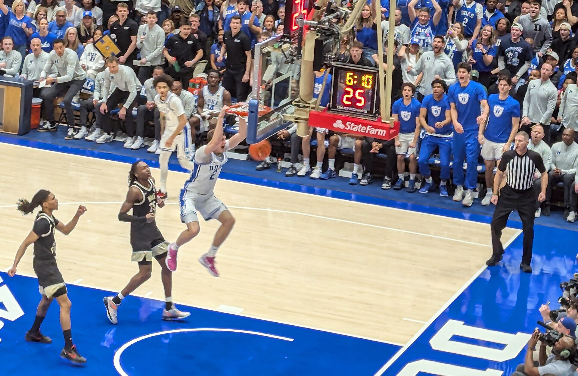 Cooper Flagg hanging on the rim after a dunk while two Wake Forest defenders look on